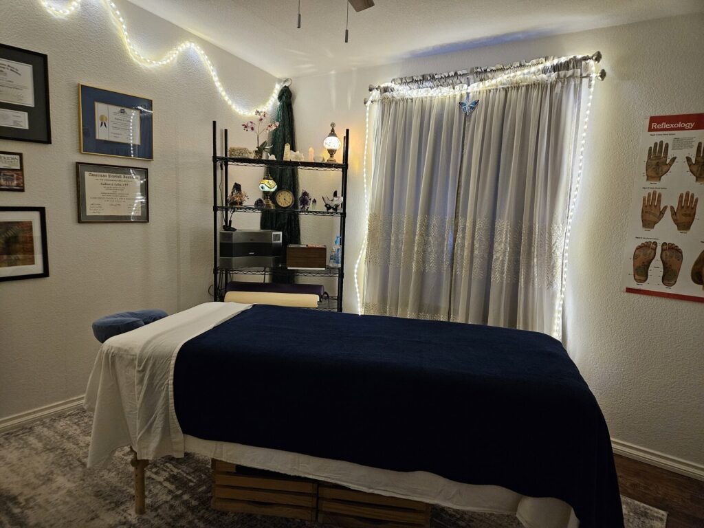 Kathi’s treatment room: a massage table with navy and white linens under warm string lights